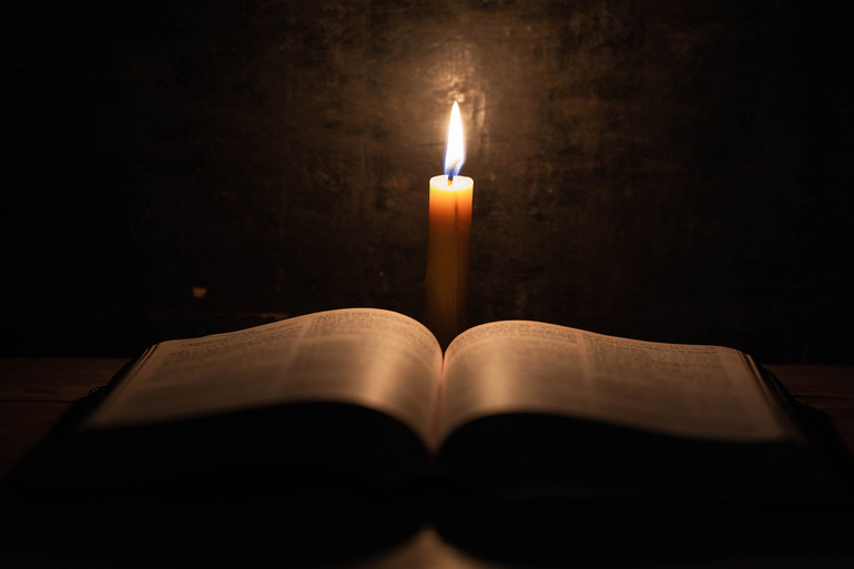 Bible and candle on a old oak wooden table.